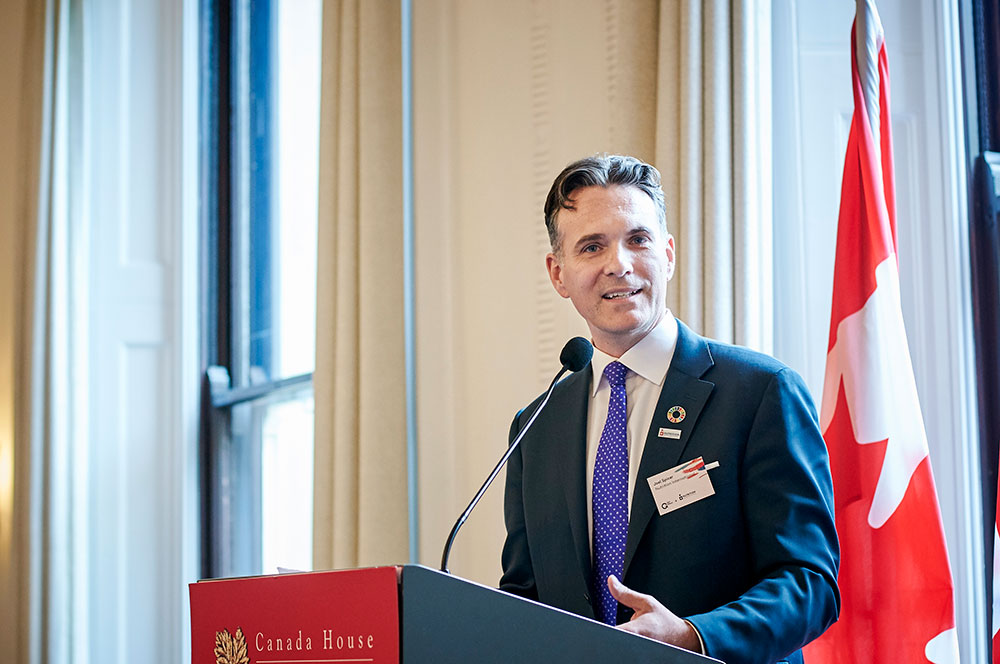 Man speaking at a podium with flags behind him