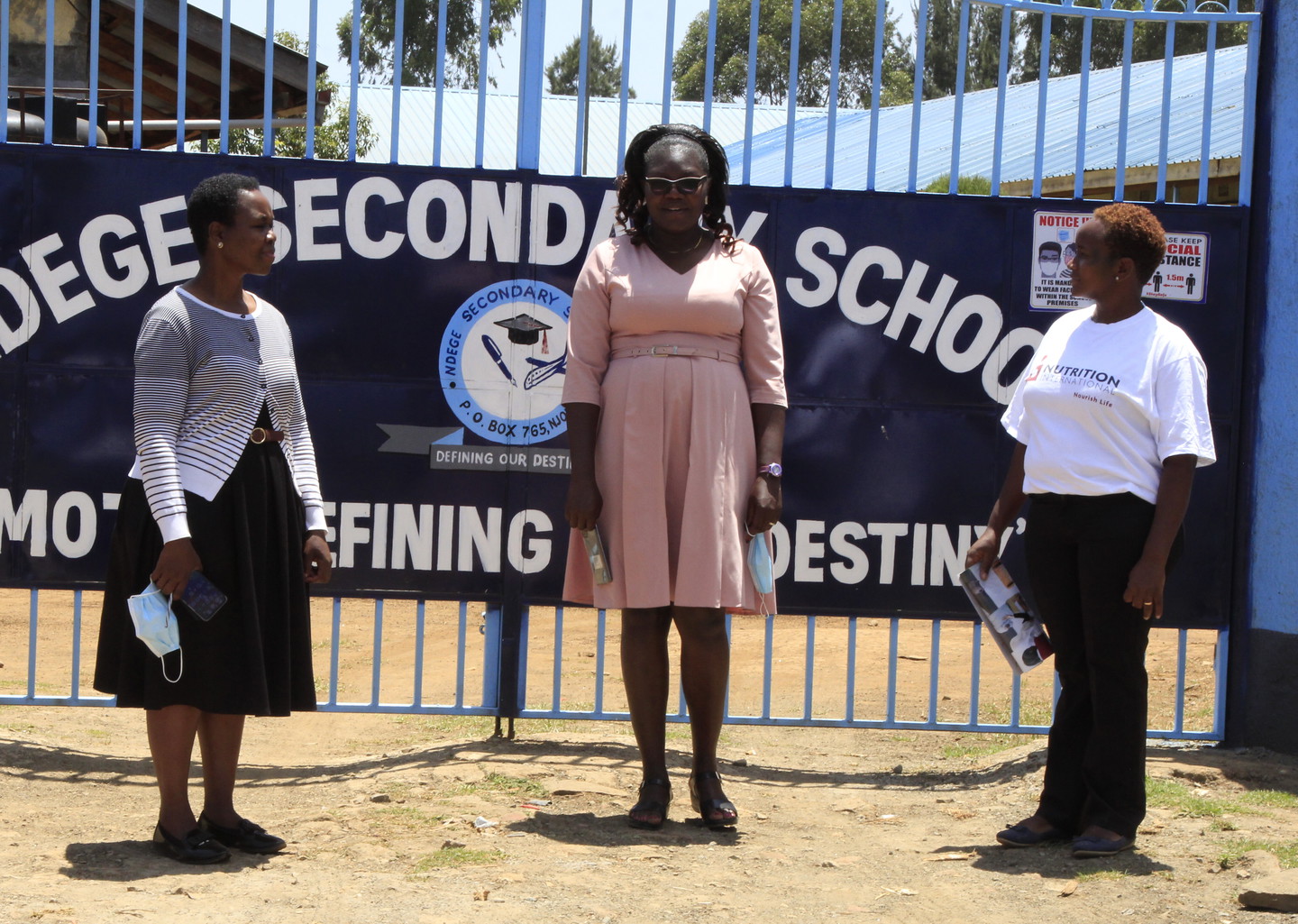 Three women standing in front of a school sign in Kenya