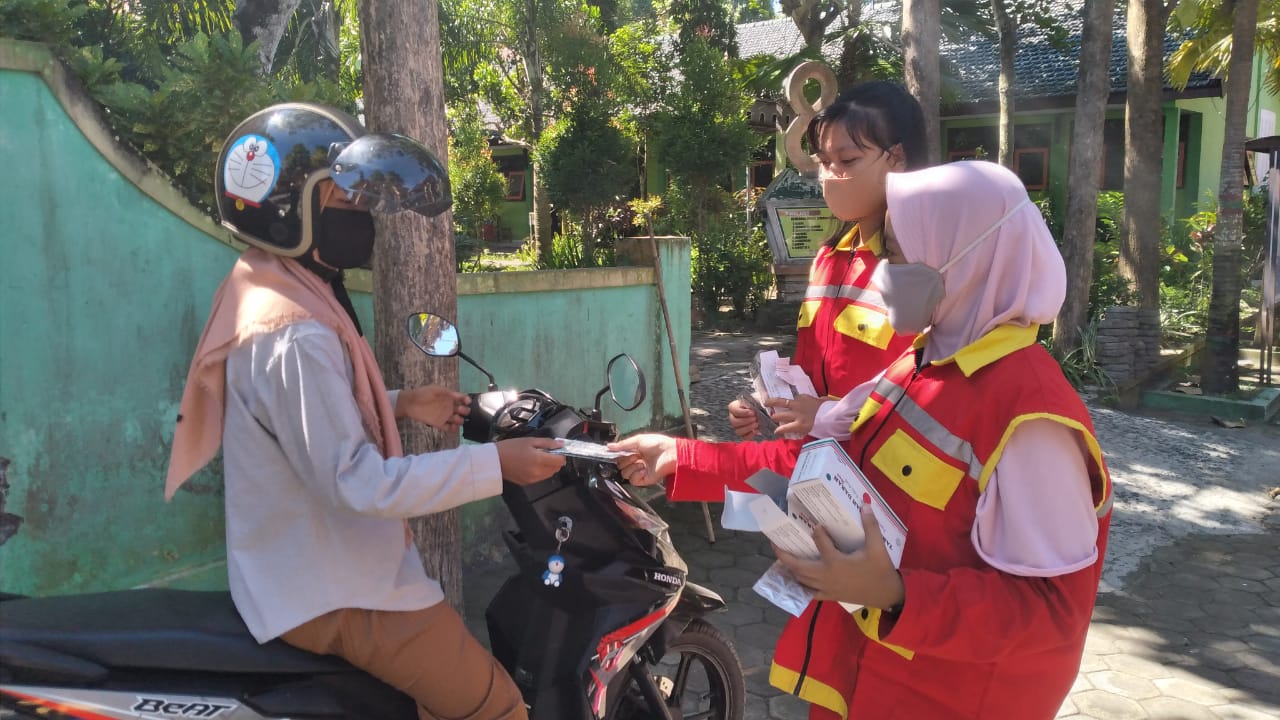 Students in vests and masks hand over supplements to a person in a mask on a motorbike