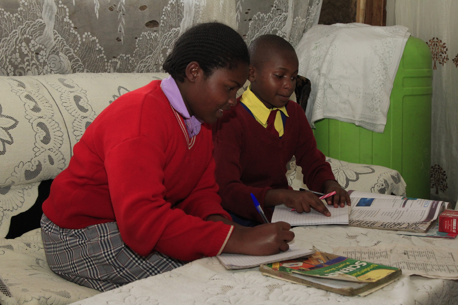 Two girls in school uniforms do their homework in their living room