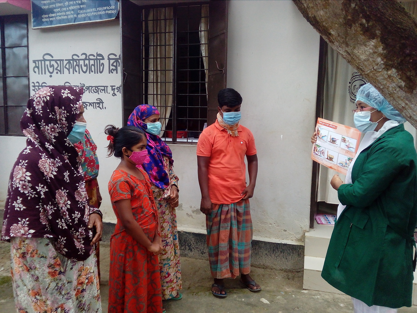 Woman in mask holds a health booklet and speaks to a group of women also in masks outside