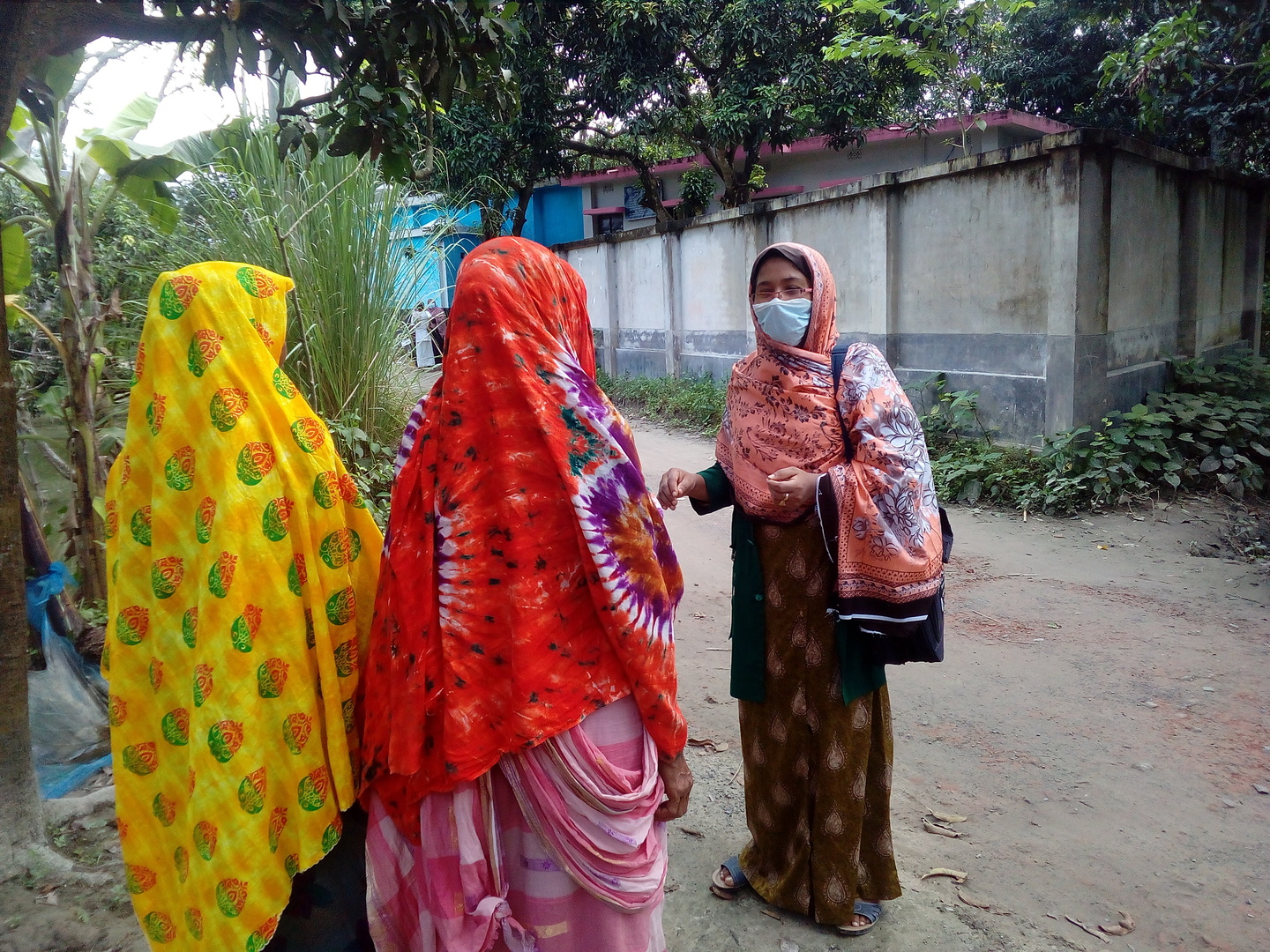 A woman in a medical mask speaks to two women on the street.