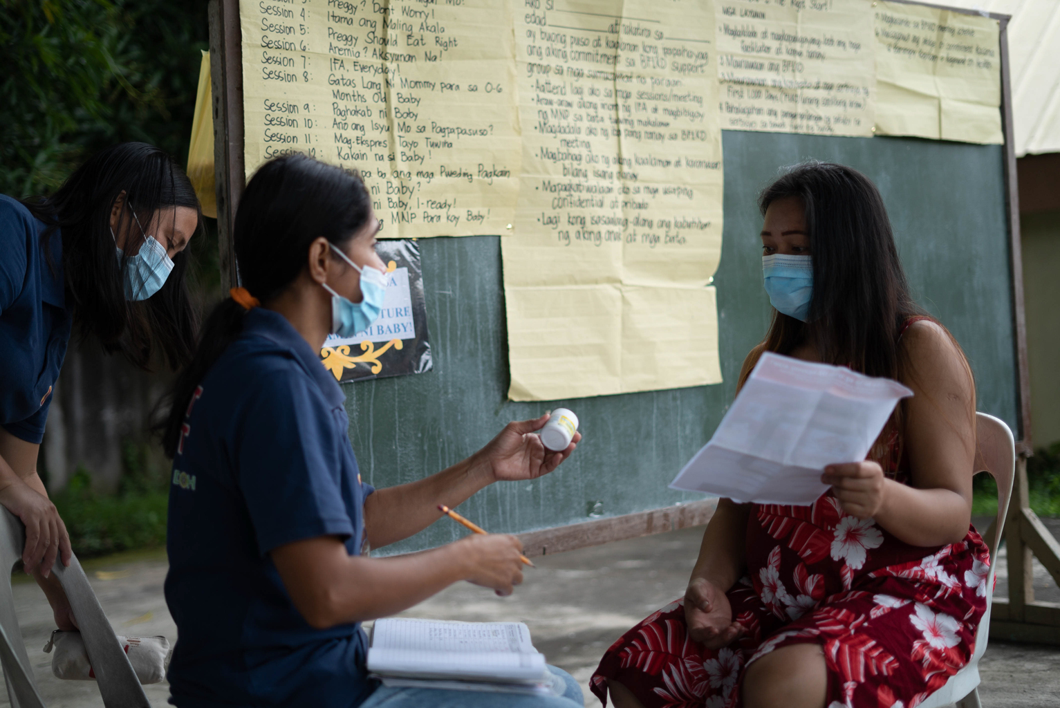 Community health volunteers speaks to a mother outside and both are wearing masks.