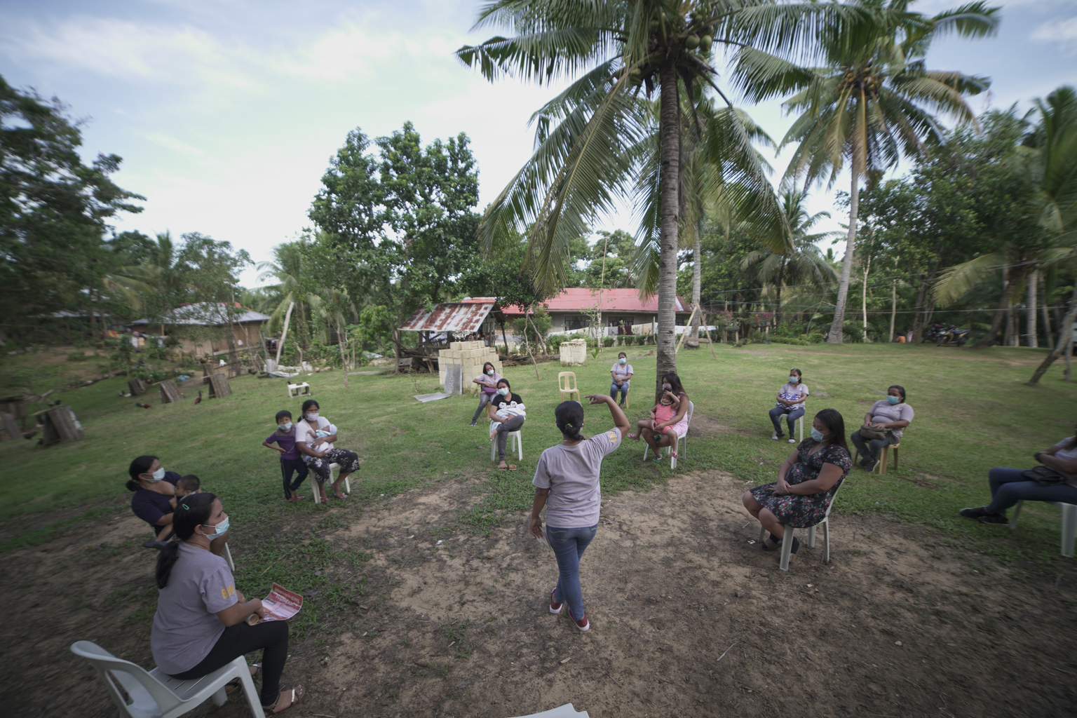 A maternal health trainers speaks to a group outside under palm trees during a mother-to-mother support group in the Philippines