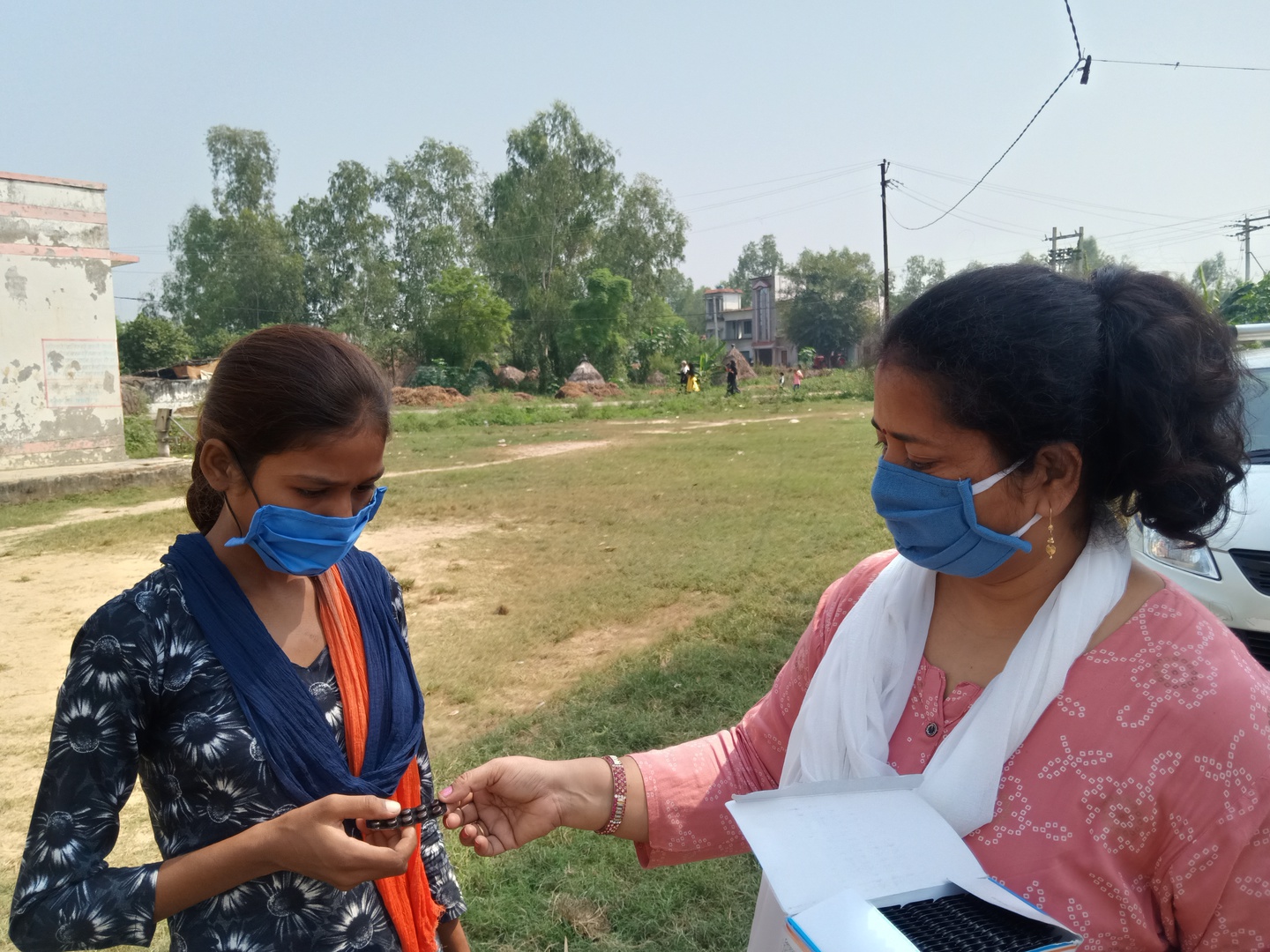 A principal in India stands to the right of a student and hands her a package of iron and folic acid supplements.