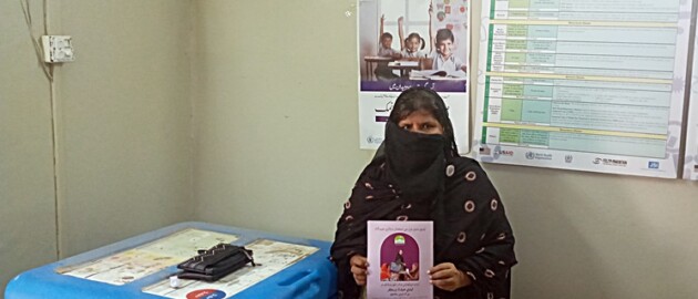 A lady health worker in Pakistan stands inside a clinic room holding a booklet on iodized salt.
