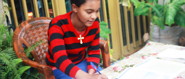 Female student leans over her homework sitting at a table surrounded by plants in Ethiopia