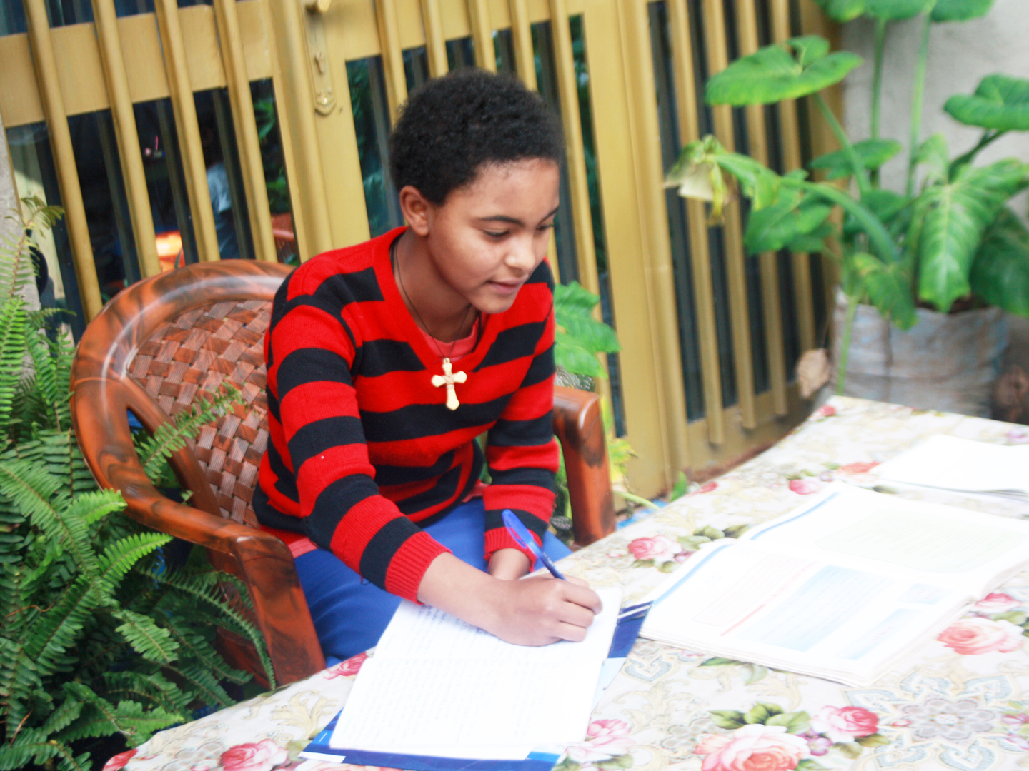 Female student leans over her homework sitting at a table surrounded by plants in Ethiopia