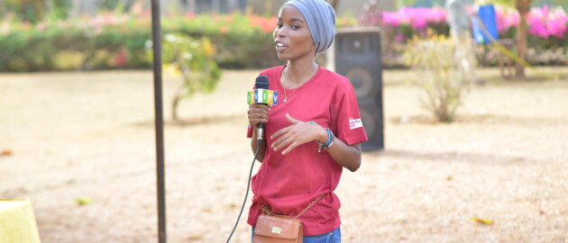 Woman standing outside holds a microphone and delivers a speech in Tanzania