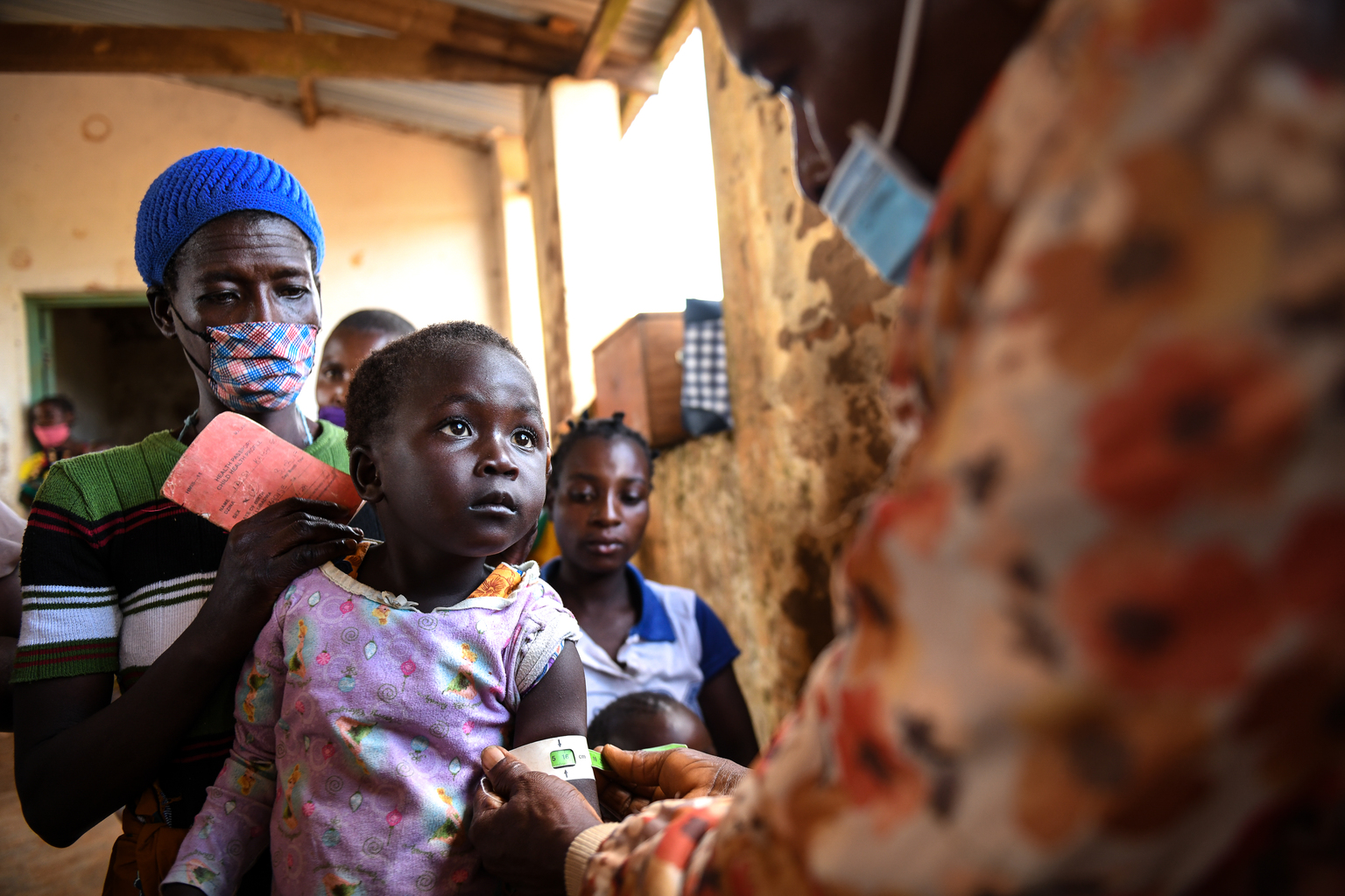 A health worker measures a young child girl growth who is sitting on her mother's lap at a health clinic in Malawi