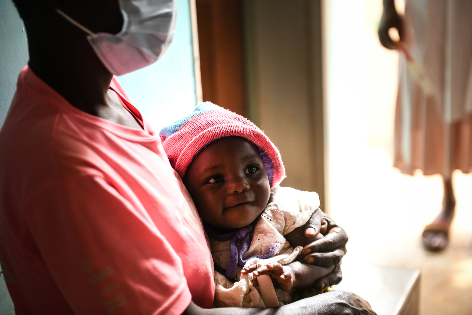 A mother wearing a mask to protect against COVID-19 holds her baby at a health clinic in Malawi