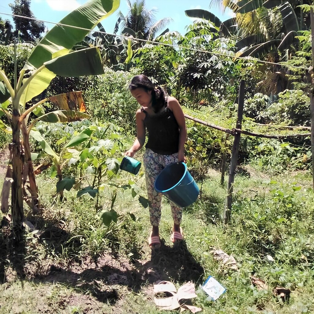 Woman standing outside watering her garden in the Philippines