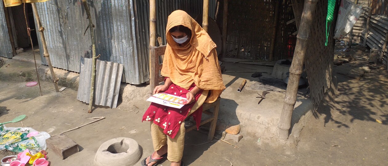 A pregnant woman dressed in a beautiful orange garmet sits by a doorstep and reads an informative pamphlet about pregnancy.