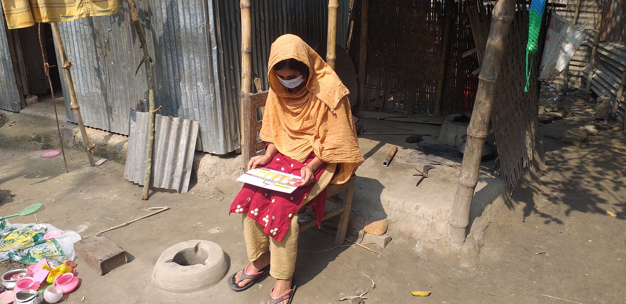 A pregnant woman dressed in a beautiful orange garmet sits by a doorstep and reads an informative pamphlet about pregnancy.