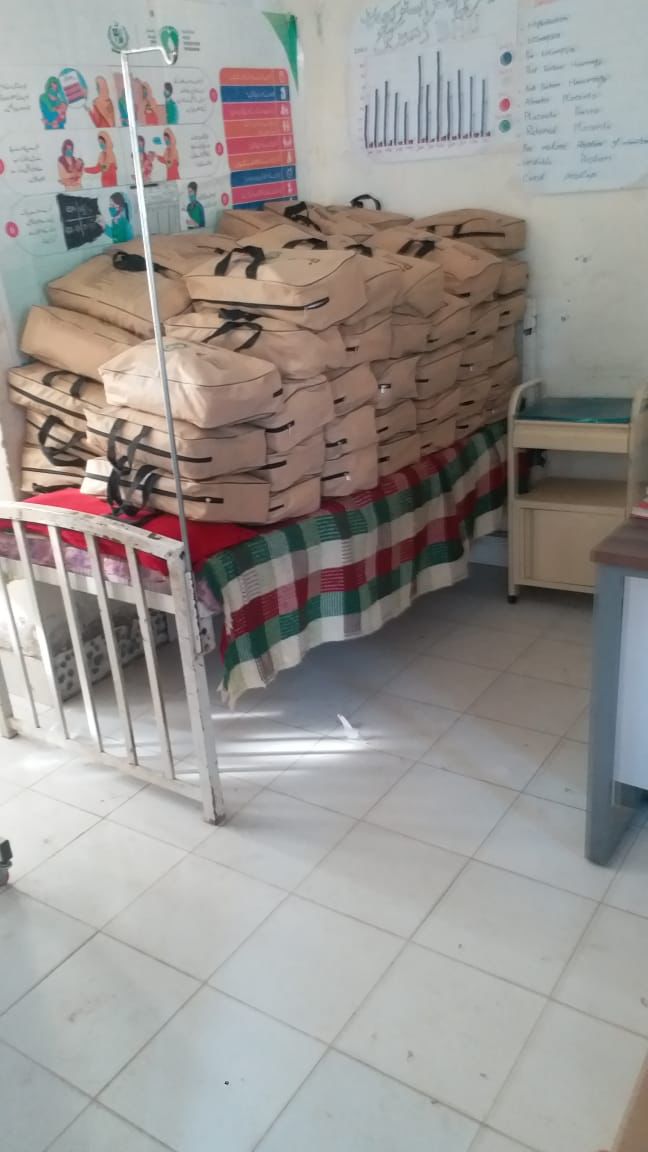 Several brown bags that are safe delivery kits are staked on a hospital bed in a medical clinic.