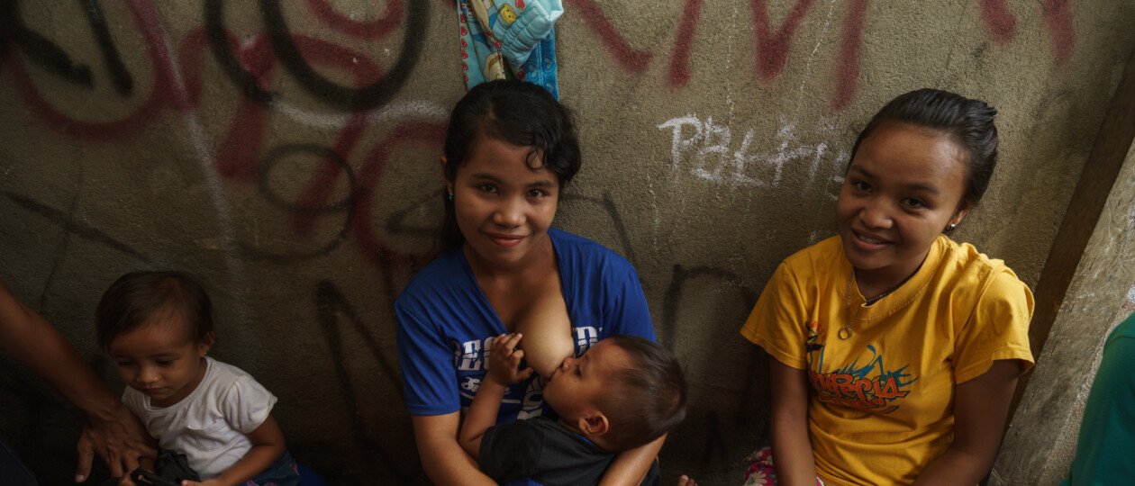 Mother in Indonesia smiling while breastfeeding baby sitting next to her two other children