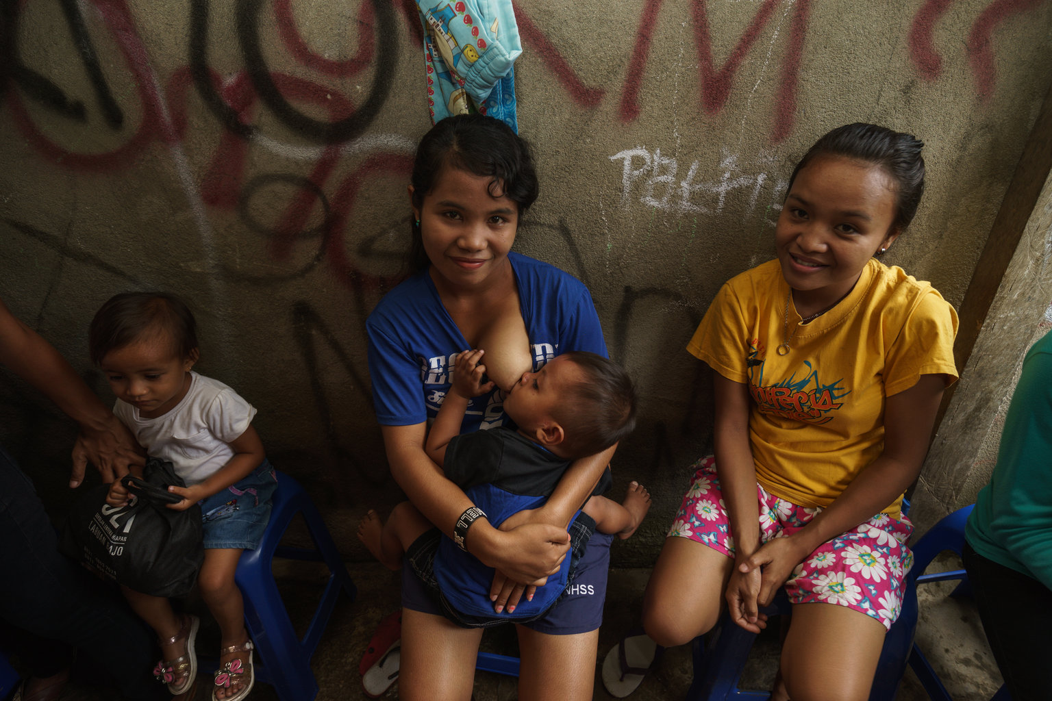 Mother in Indonesia smiling while breastfeeding baby sitting next to her two other children