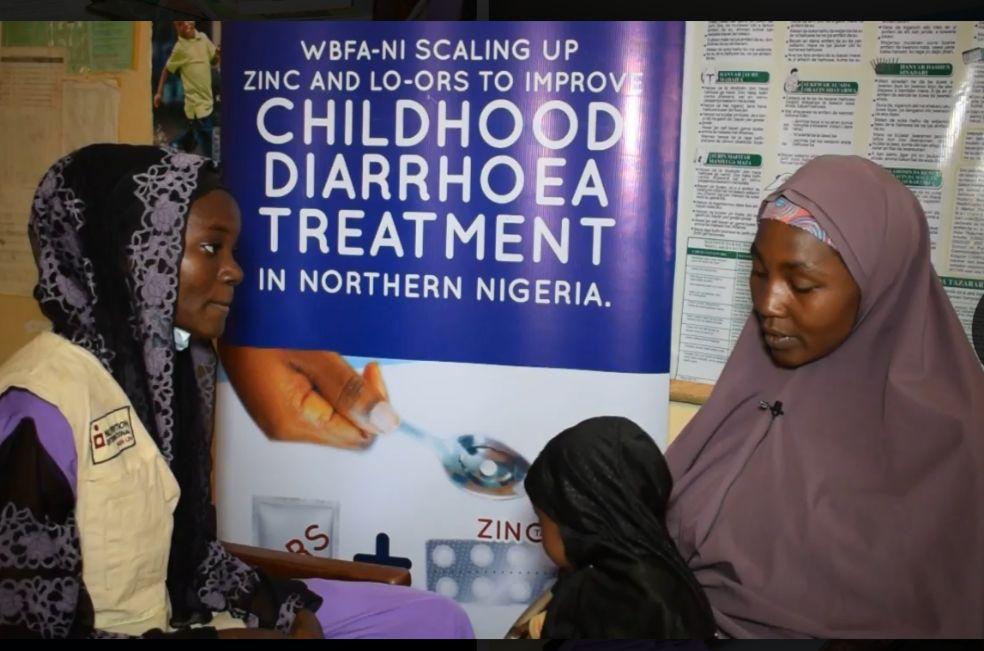 Thirty-four-year-old mother sits inside a a health centre with her fifteen-month-old-baby on her lap as a health worker sits beside her and counsells her on diarrhoea management and zinc and LO-ORS treatment.