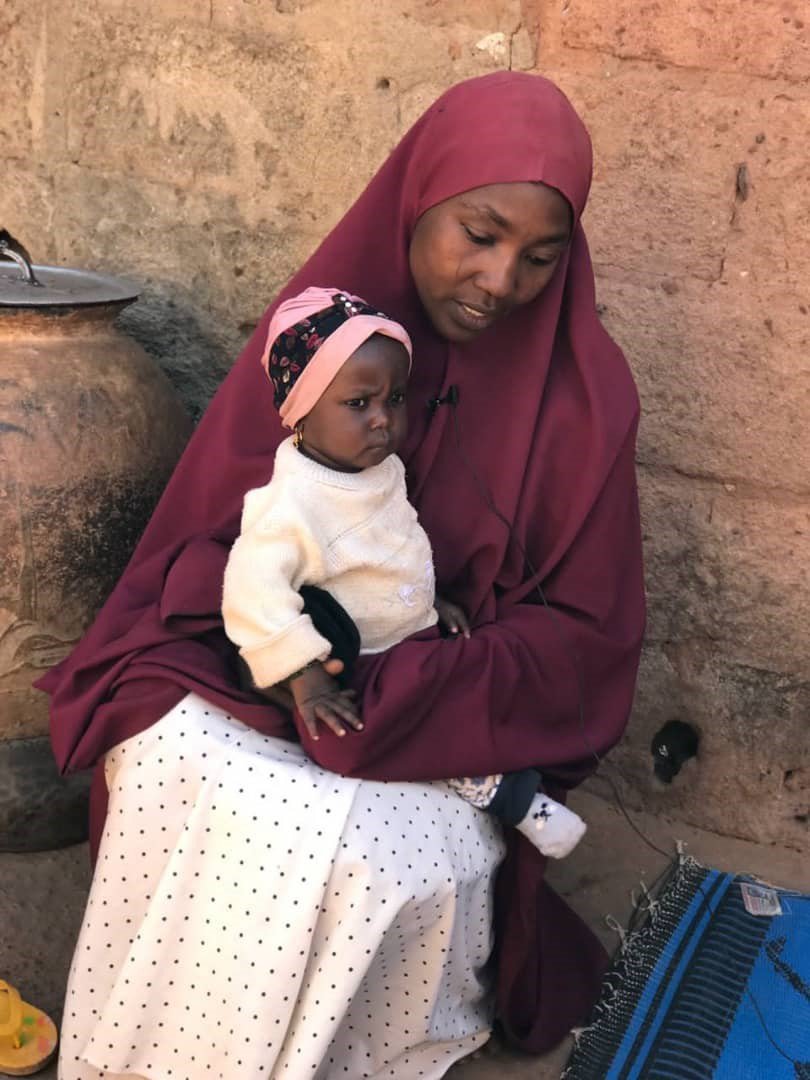 Une mère de trente-quatre ans est assise devant un immeuble avec son bébé de quinze mois posé sur ses genoux.