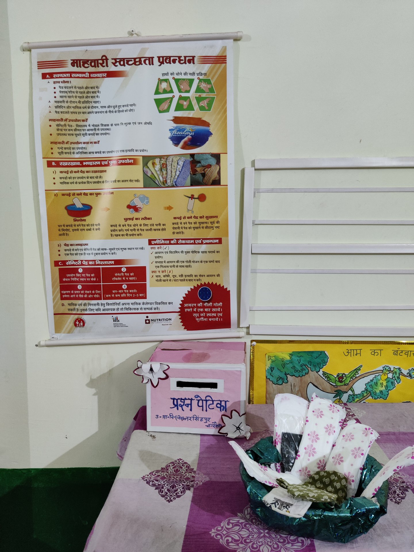 L’initiative met des serviettes hygiéniques menstruelles à la disposition des adolescentes sur une table, dans un panier, devant une affiche qui fournit des informations éducatives sur les règles.