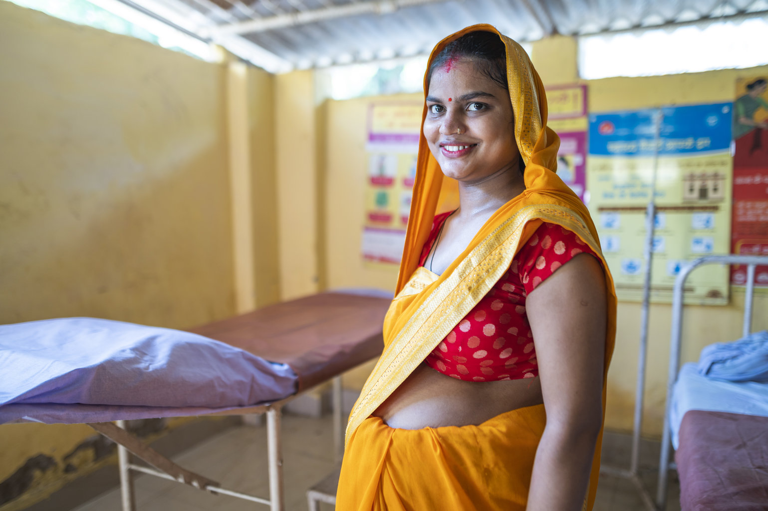 a smiling pregnant woman stands in a room by an hospital bed