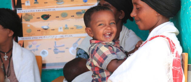 A mother stares smiling at her child who is laughing and looking at the camera.