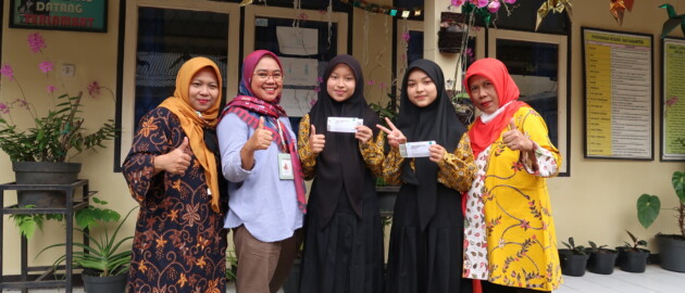 A group of students and teachers smile at the camera and hold up packages of weekly iron and folic acid supplementation.