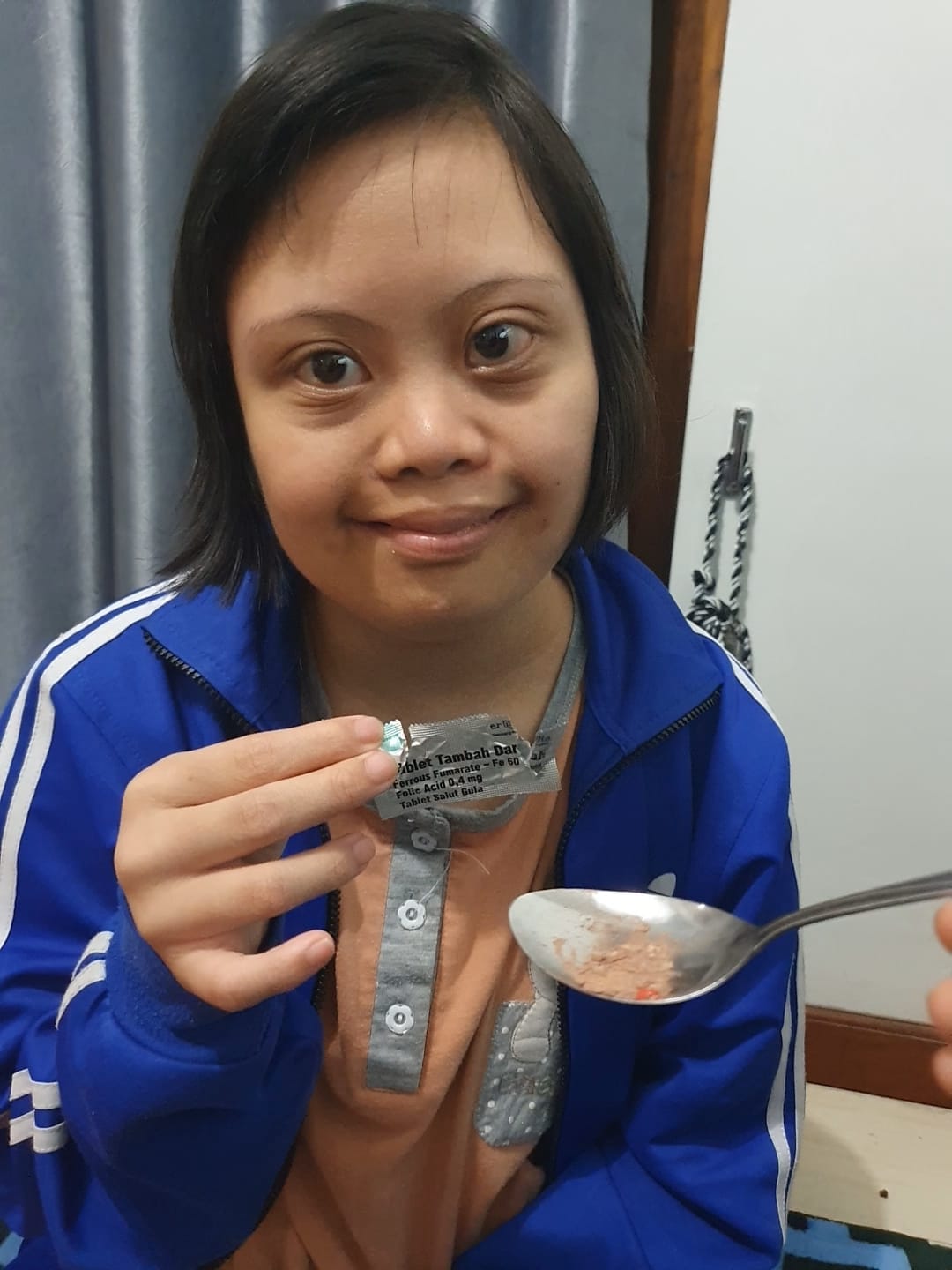 An adolescent girl smiles to camera holding a packet of weekly iron and folic acid supplementation.