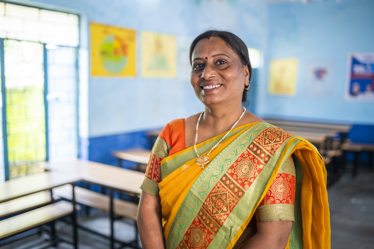 A woman in an orange sari stands smiling 