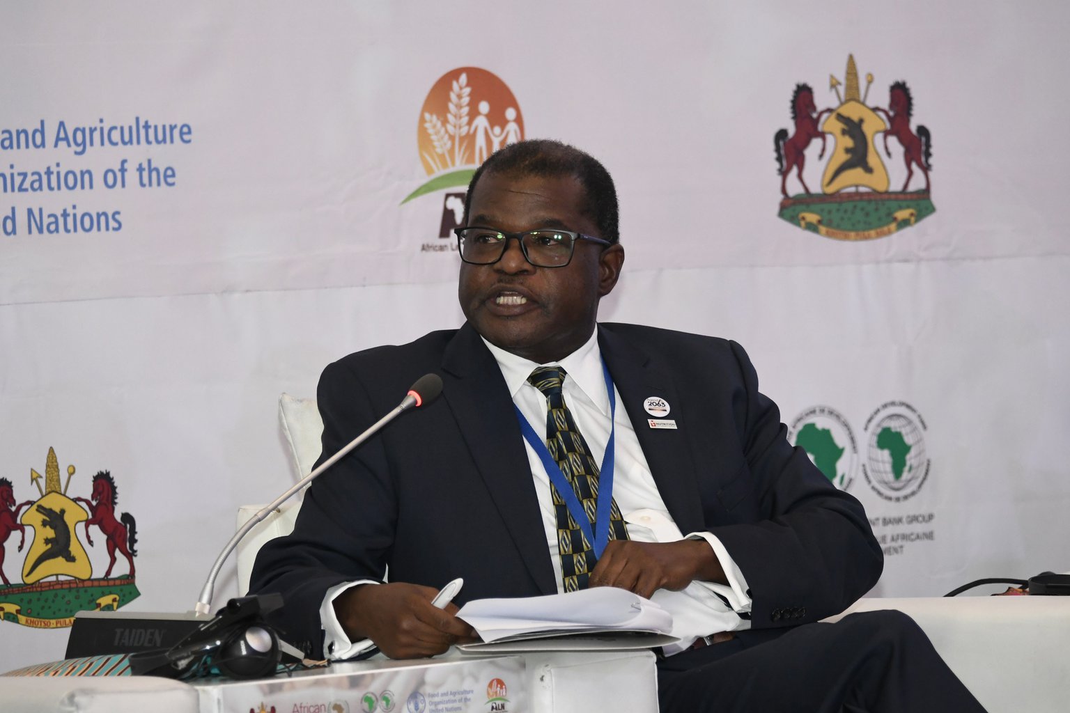 A man sits facing the camera holding a microphone