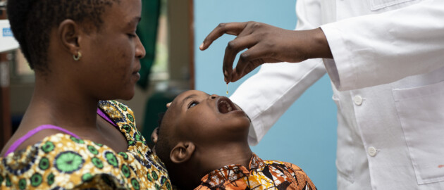 A mother holder her child who has their mouth open as they receive a dose of vitamin A.