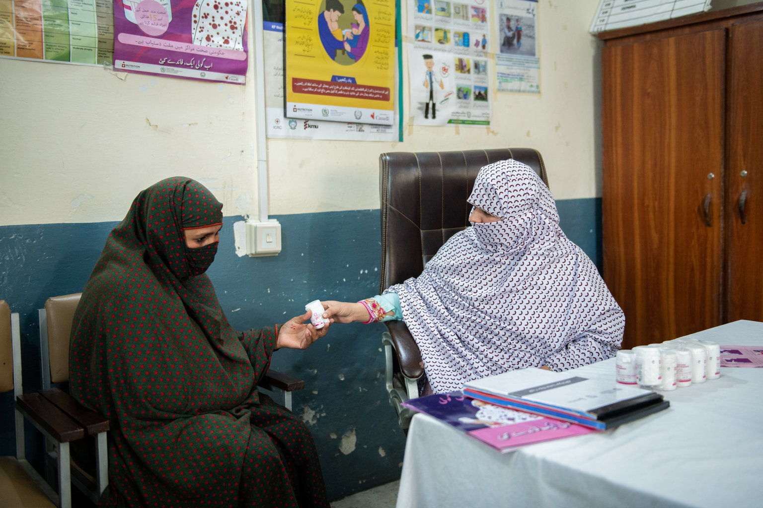 A woman passing a bottle of tablets to another woman