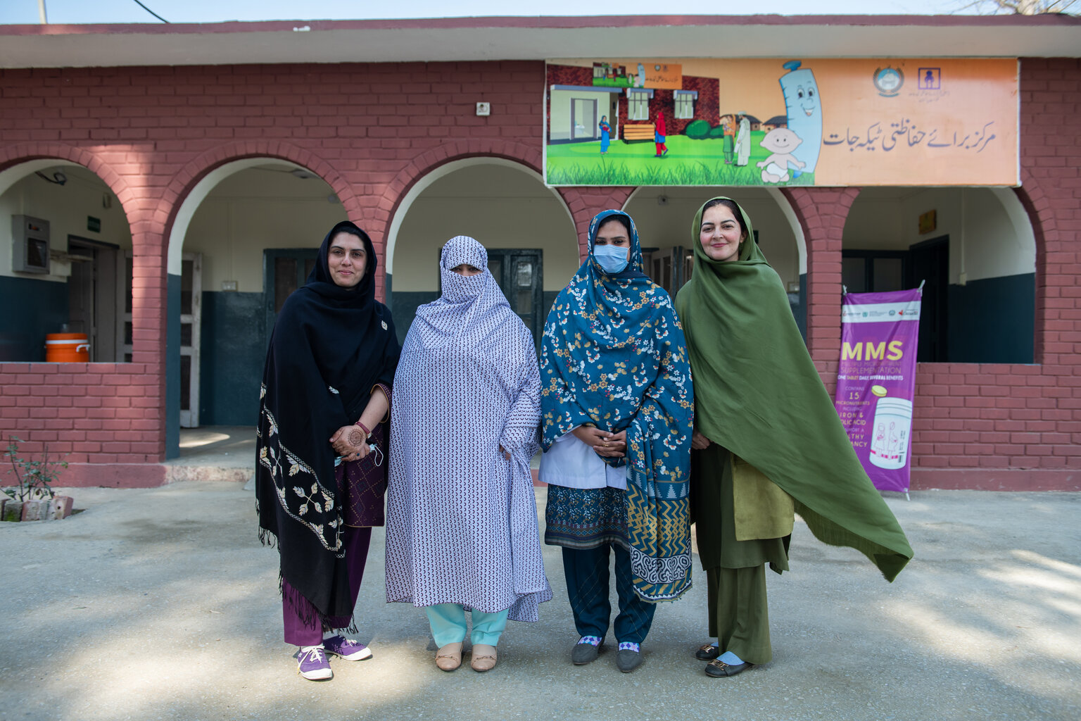 Four woman stand beside each other outside a health centre looking at the camera.