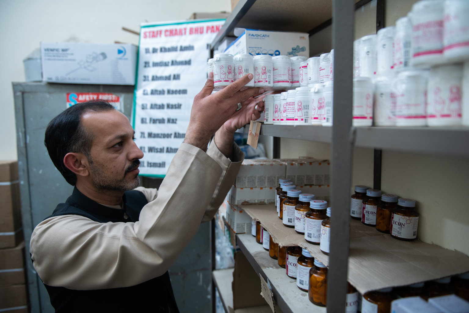 A man lifts a package of supplementation bottles onto a shelf.