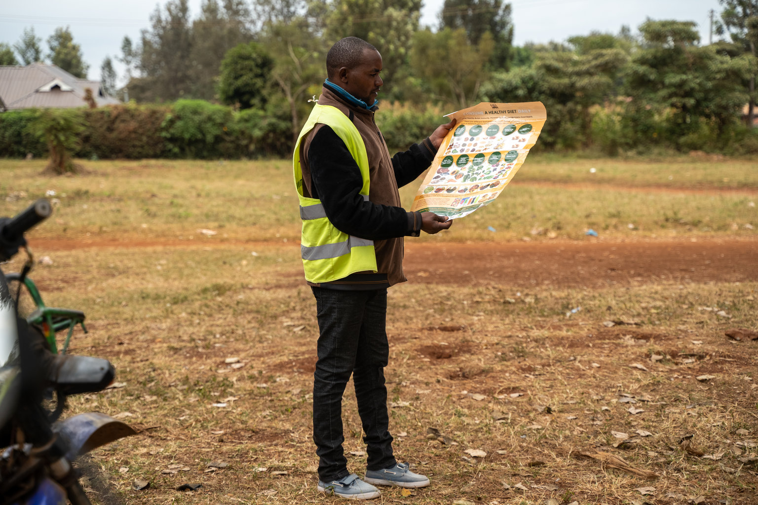 A man wearing a yellow vest hold up an instructional poster.