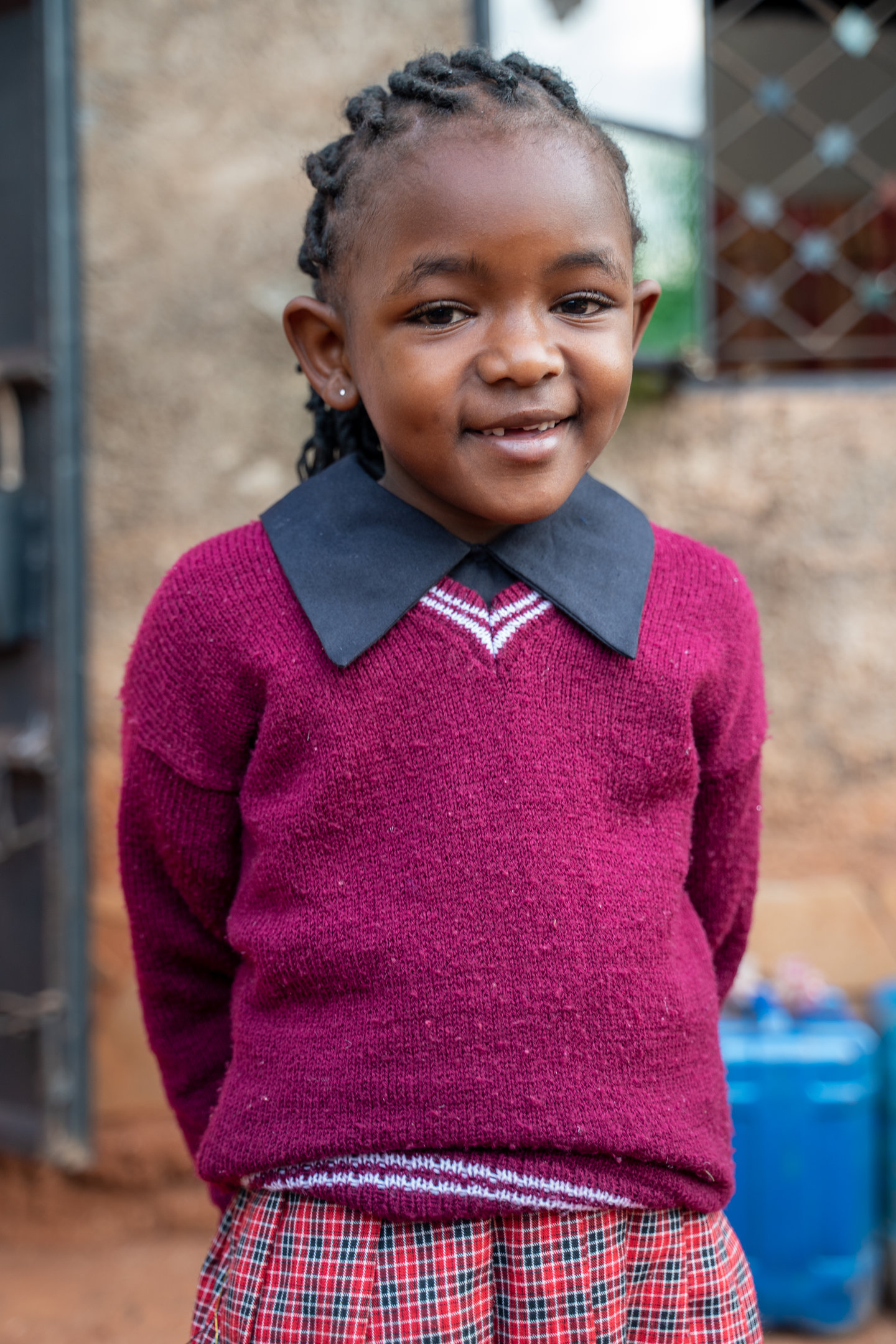 A young girl in a school uniform smiles and looks at the camera.