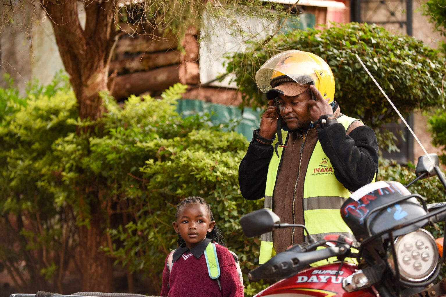  Un homme met un casque de moto alors qu’il s’apprête à partir au travail. Il se tient à côté d’une jeune fille en uniforme scolaire qui quitte aussi son domicile pour la journée.
