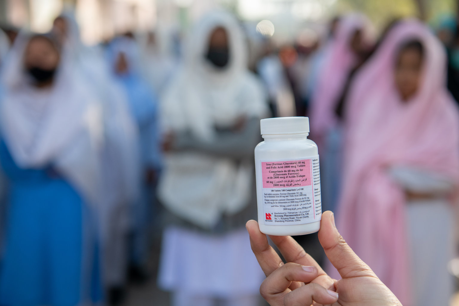 A hand holds a bottle of pills for weekly iron and folic acid supplementation