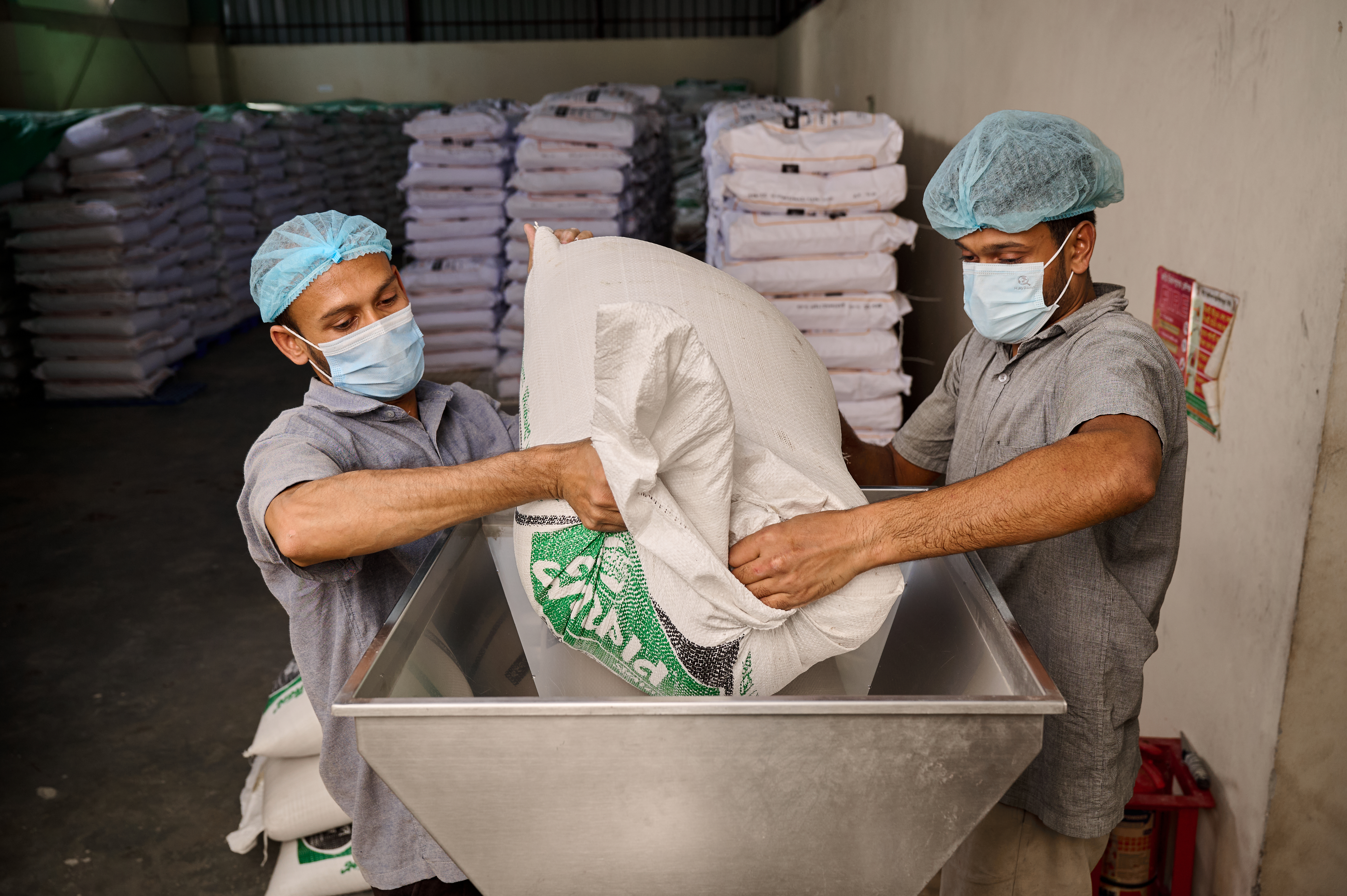 Two workers load a micronutrient premix into a metal container.
