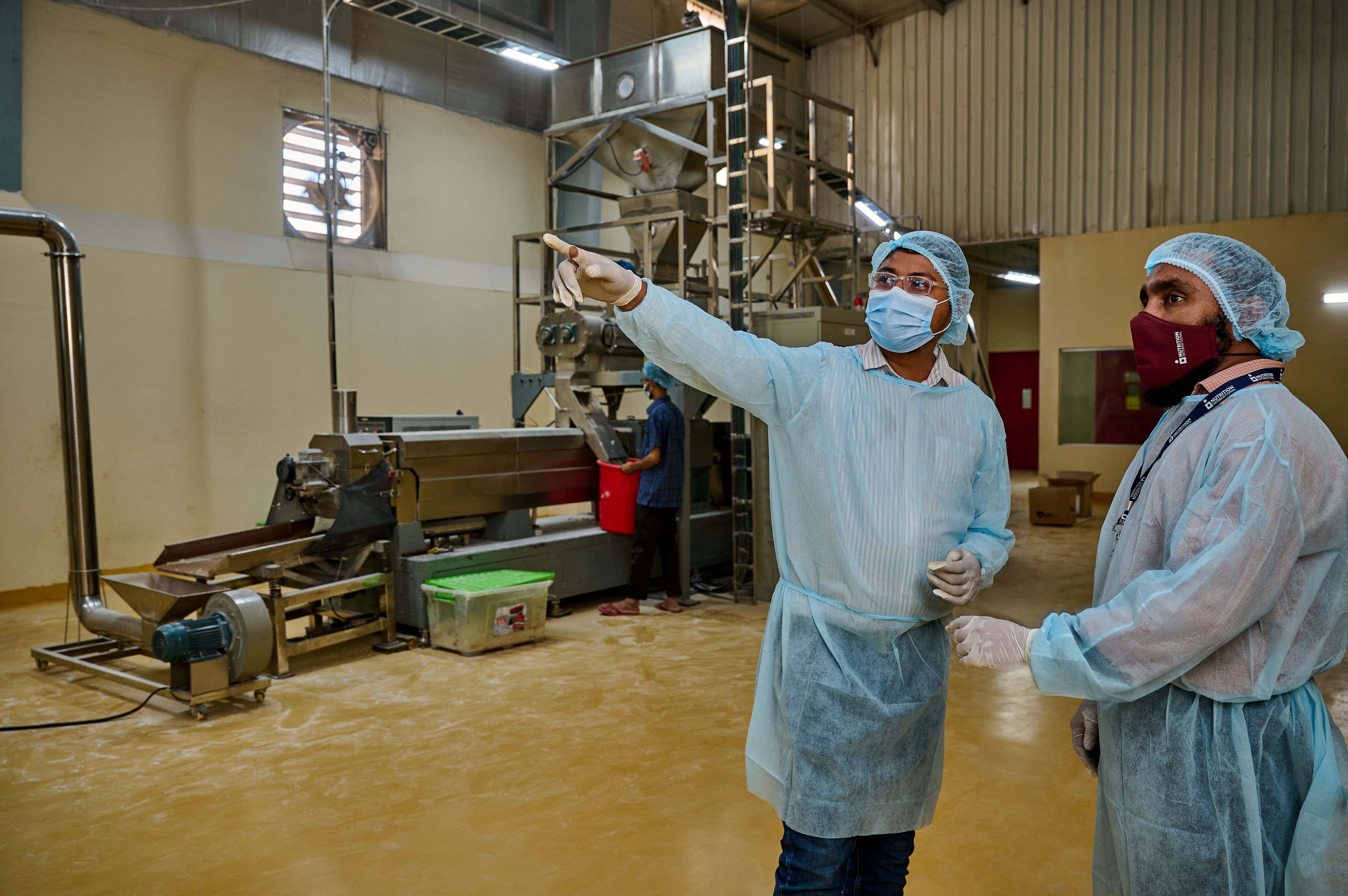 Two workers stand in the middle of a factory floor, on a montioring and quality assurance visit.