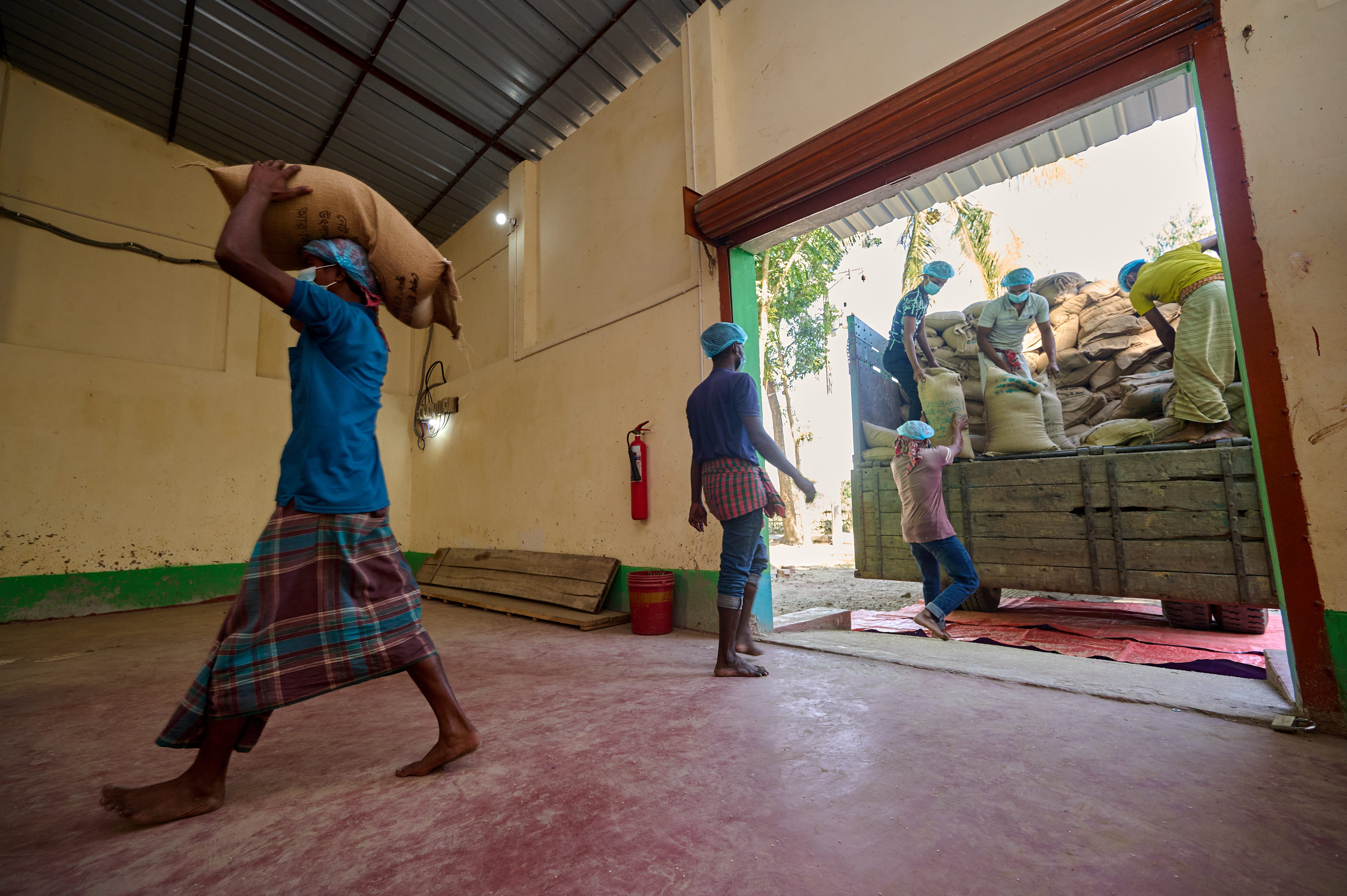 Workers carry sacks of non-fortified rice into a rice fortification blending facility in Jamalpur, Bangladesh.