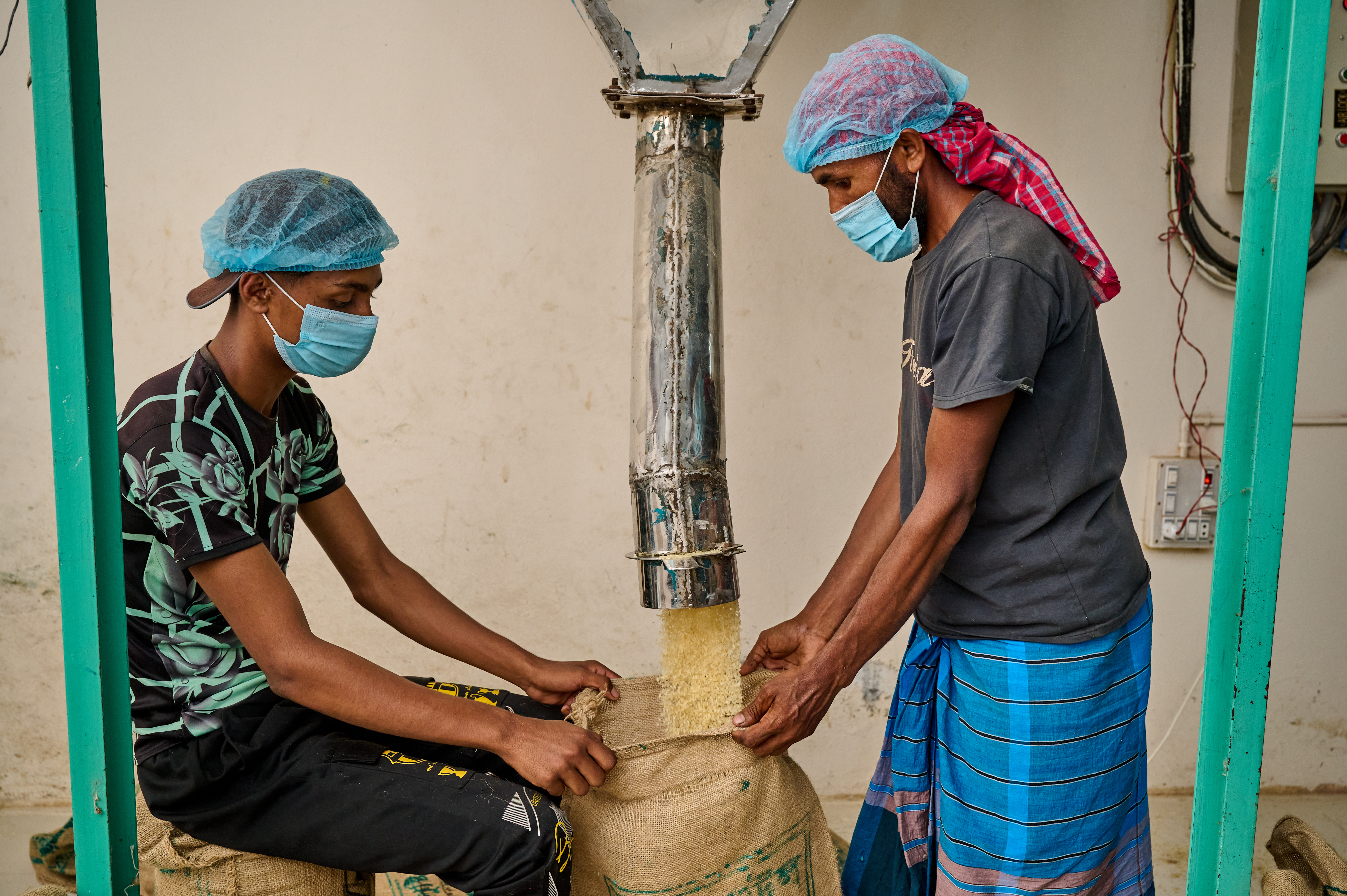 Two workers hold a sack that blended fortitied rice kernals and nonfortified kernals are combined into in Bangladesh.