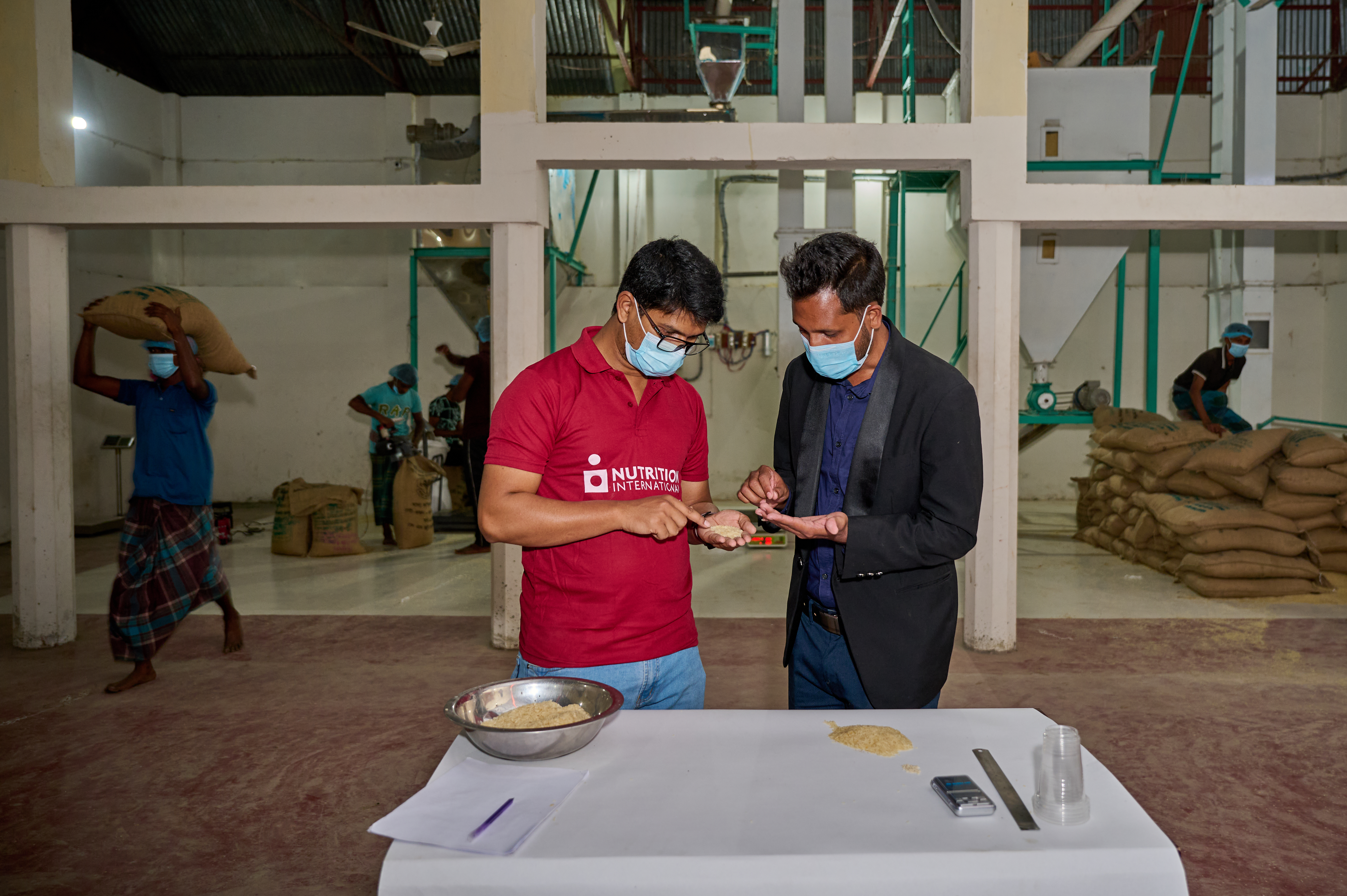 Two people perform a quality assurance check to ensure the ratio between fortified rice kernals and non-fortified kernals are appropraitely blended at a facility in Bangladesh. 