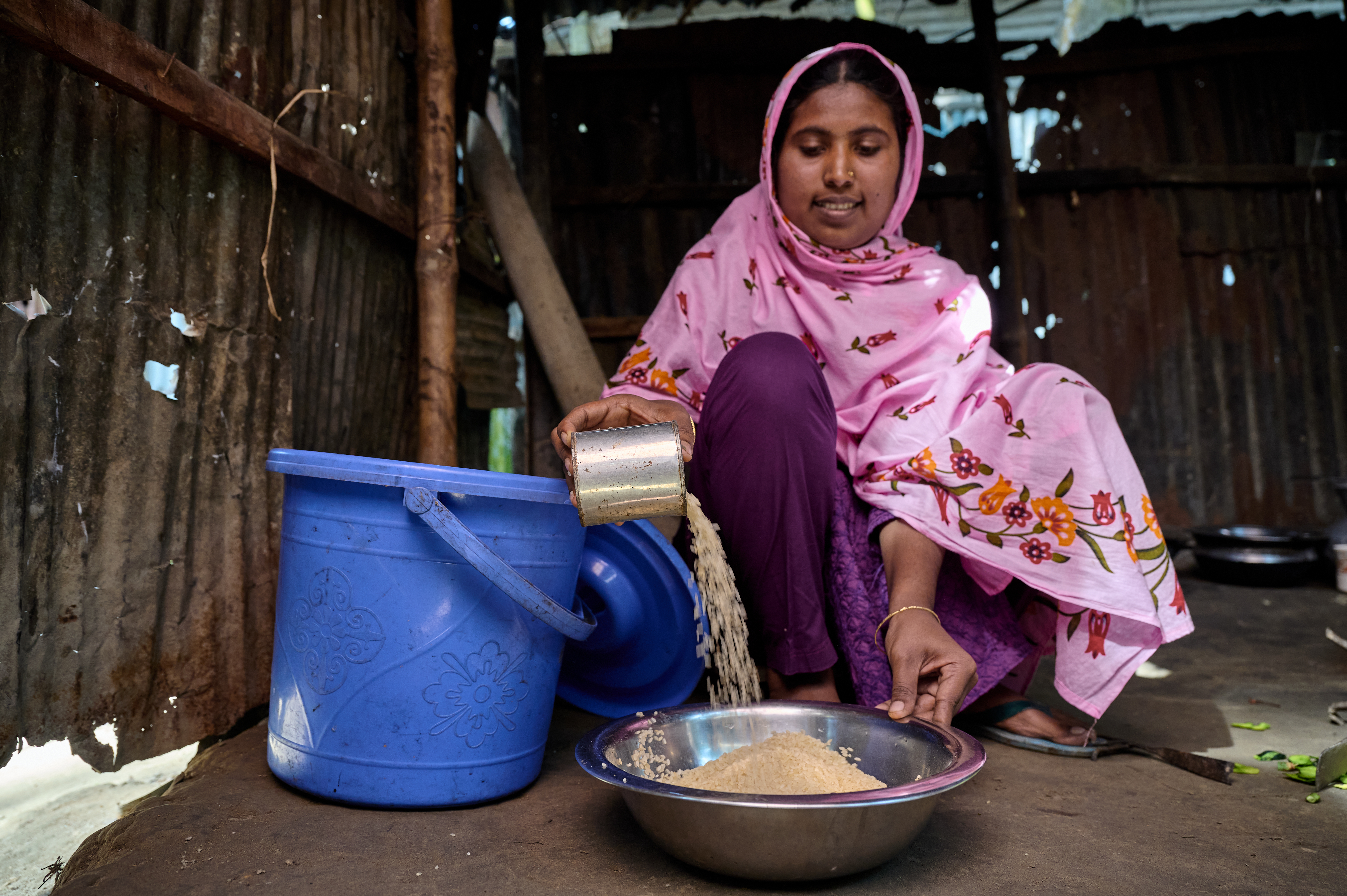 A woman measure rices by pouring it into a bowl. The kernals are a cascading waterfall and build up a mound. 