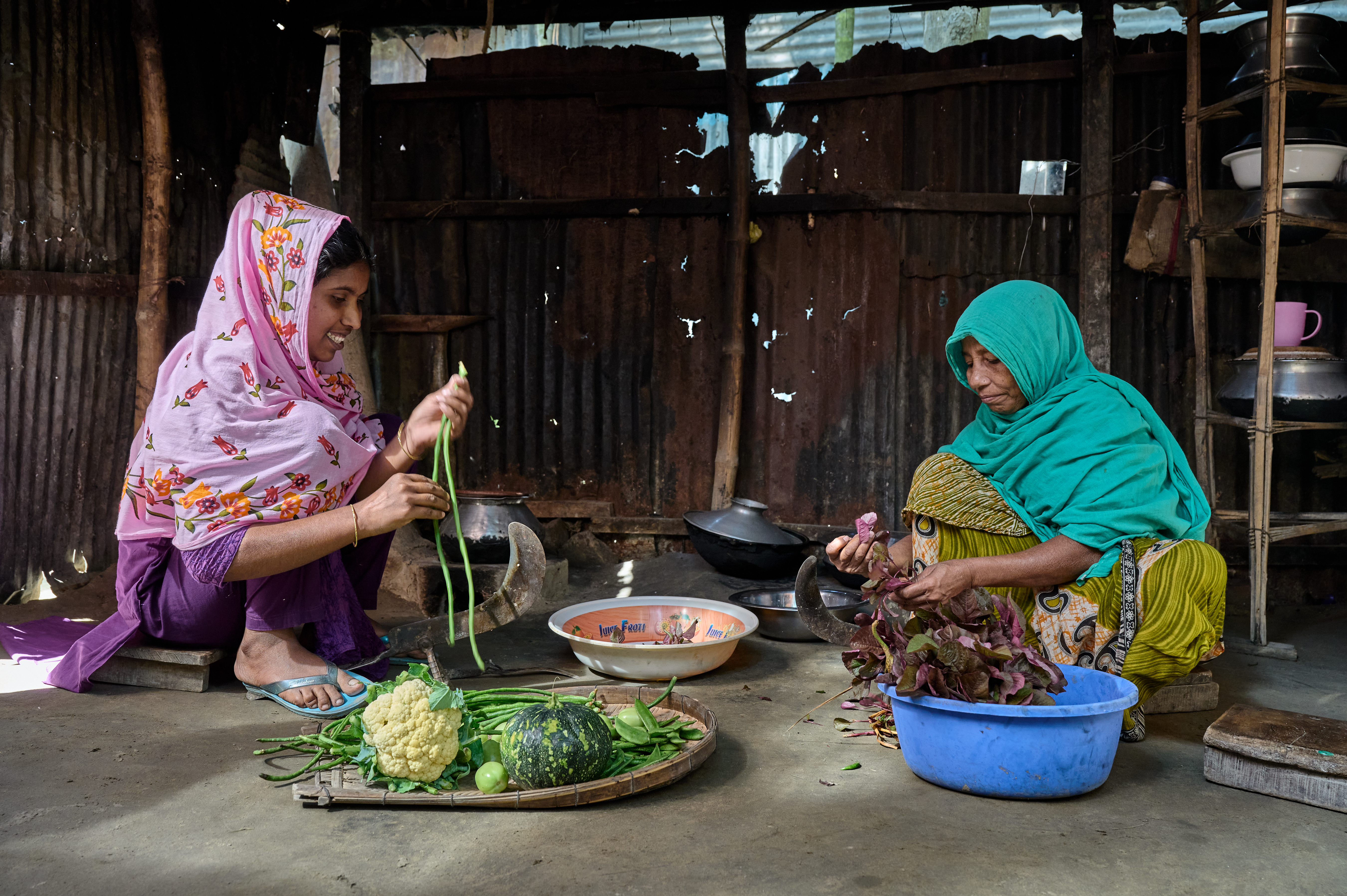 Two women prepare the midday meal together. Rice is the common base for meals, and they are preparing vegetable curry to accompany it.