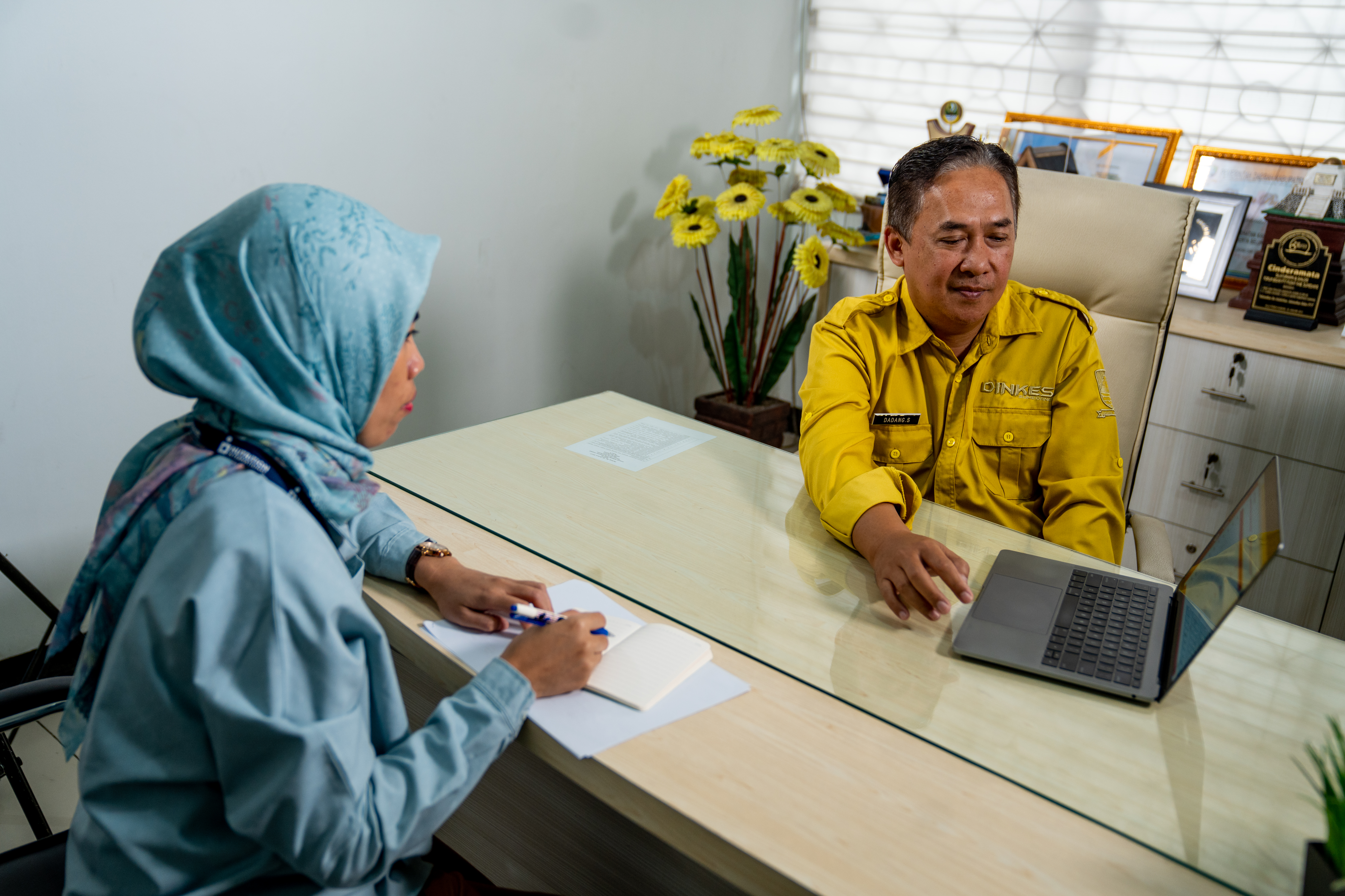 A man sits across a table from a woman and points at an electronic screen