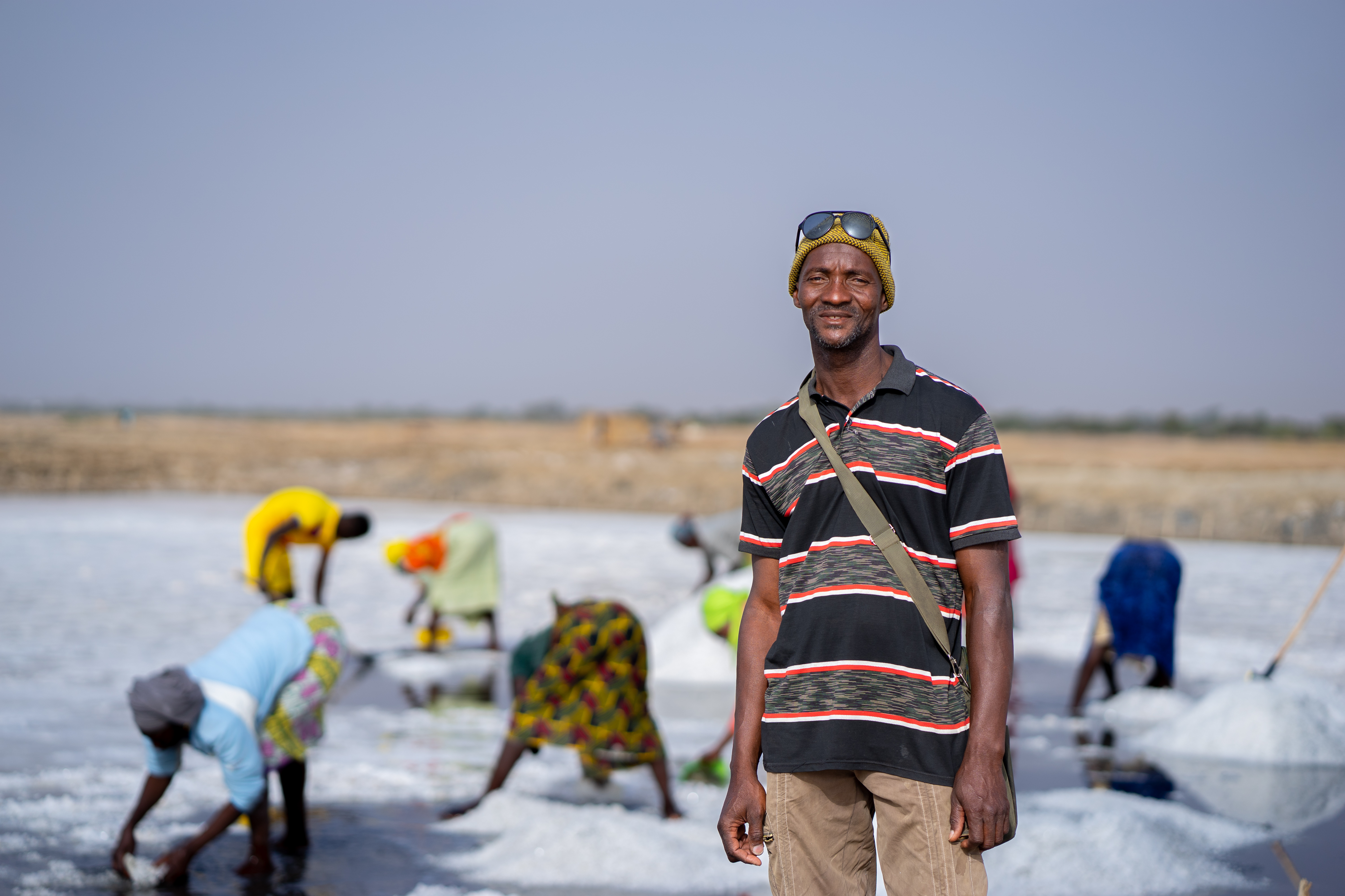 A man looks to the camera with the background of people working on a salt field.