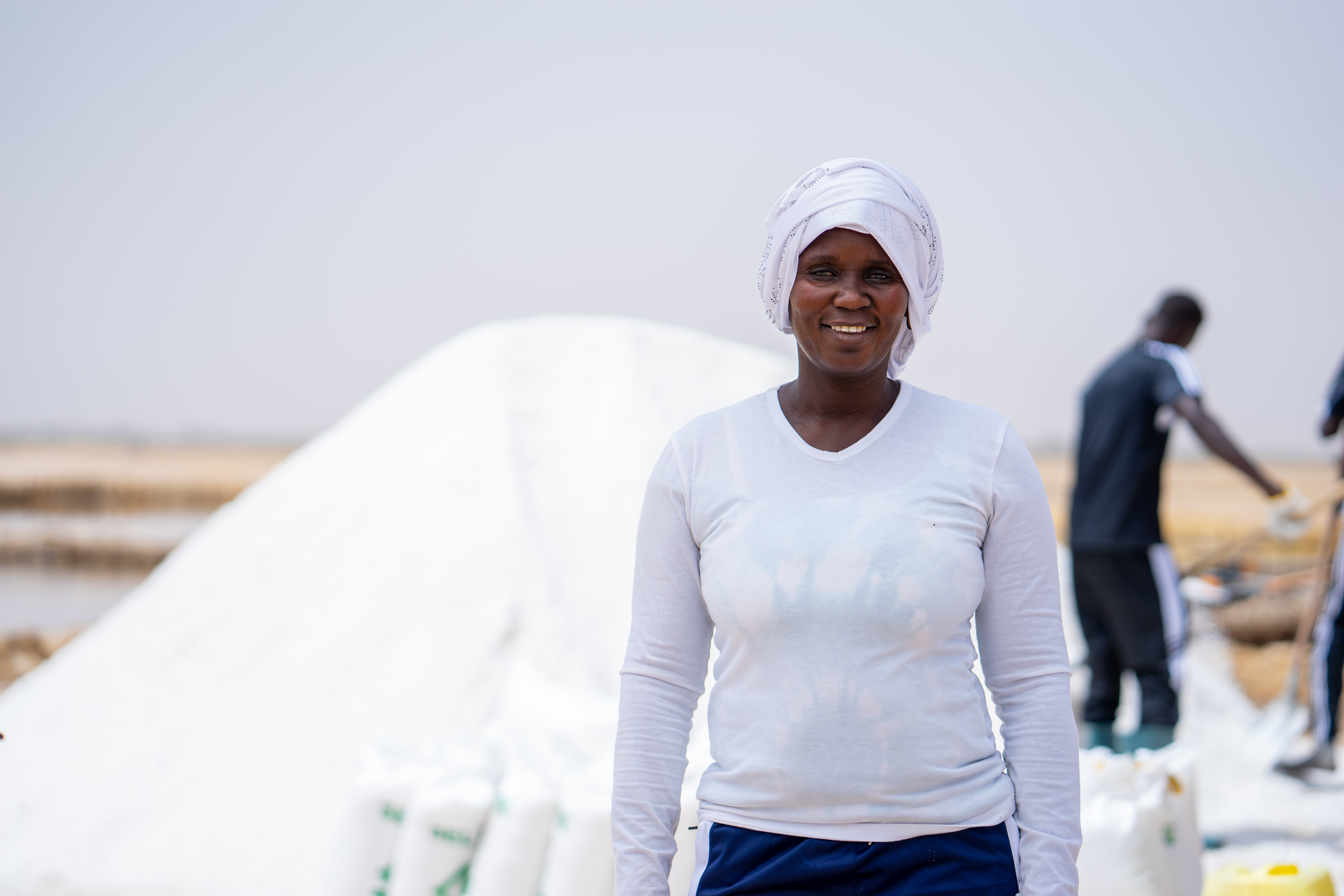 A woman smiles to the camera with a large mound of salt behind her.