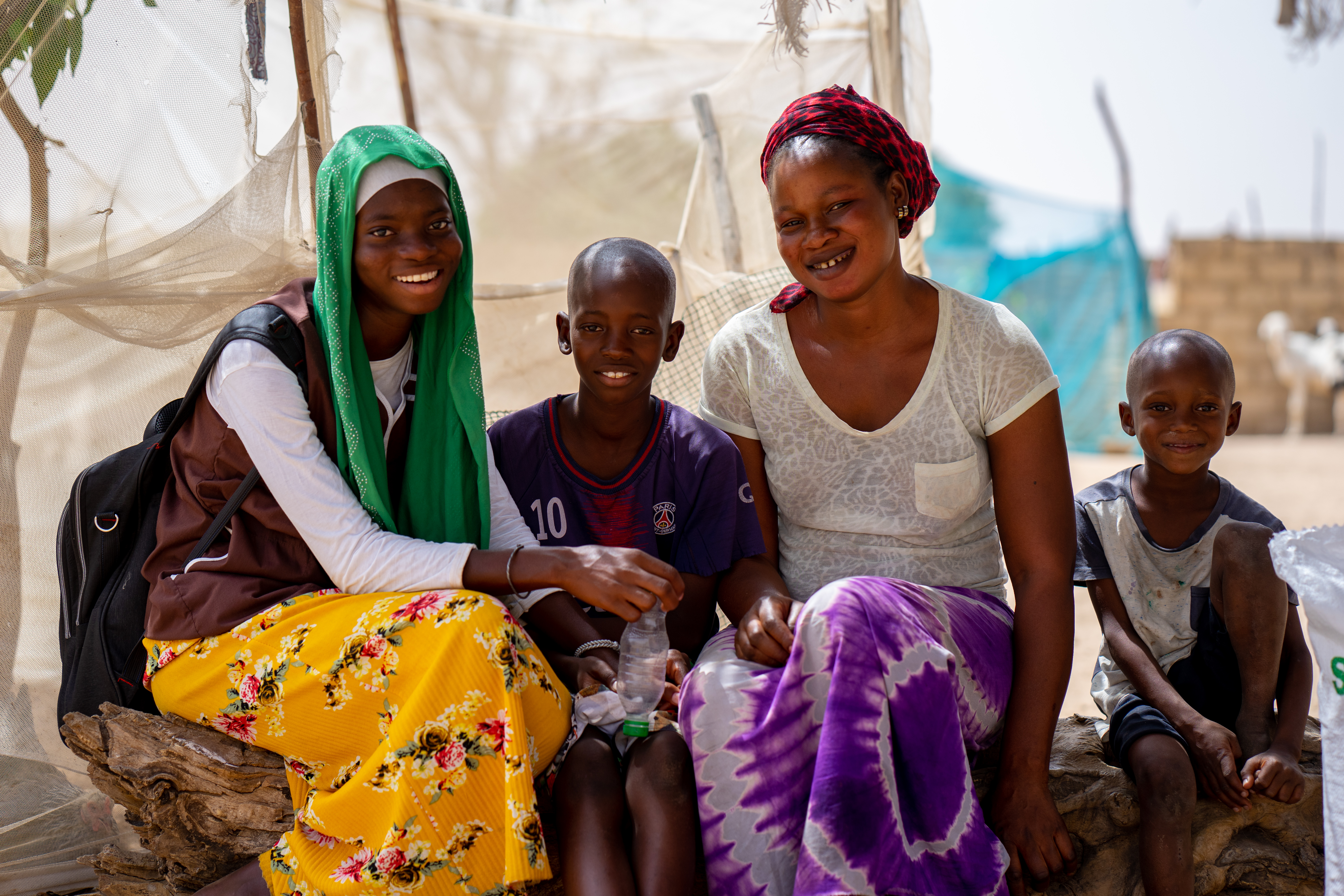 A mother sits beside her three children. They are all looking at the camera and smiling.