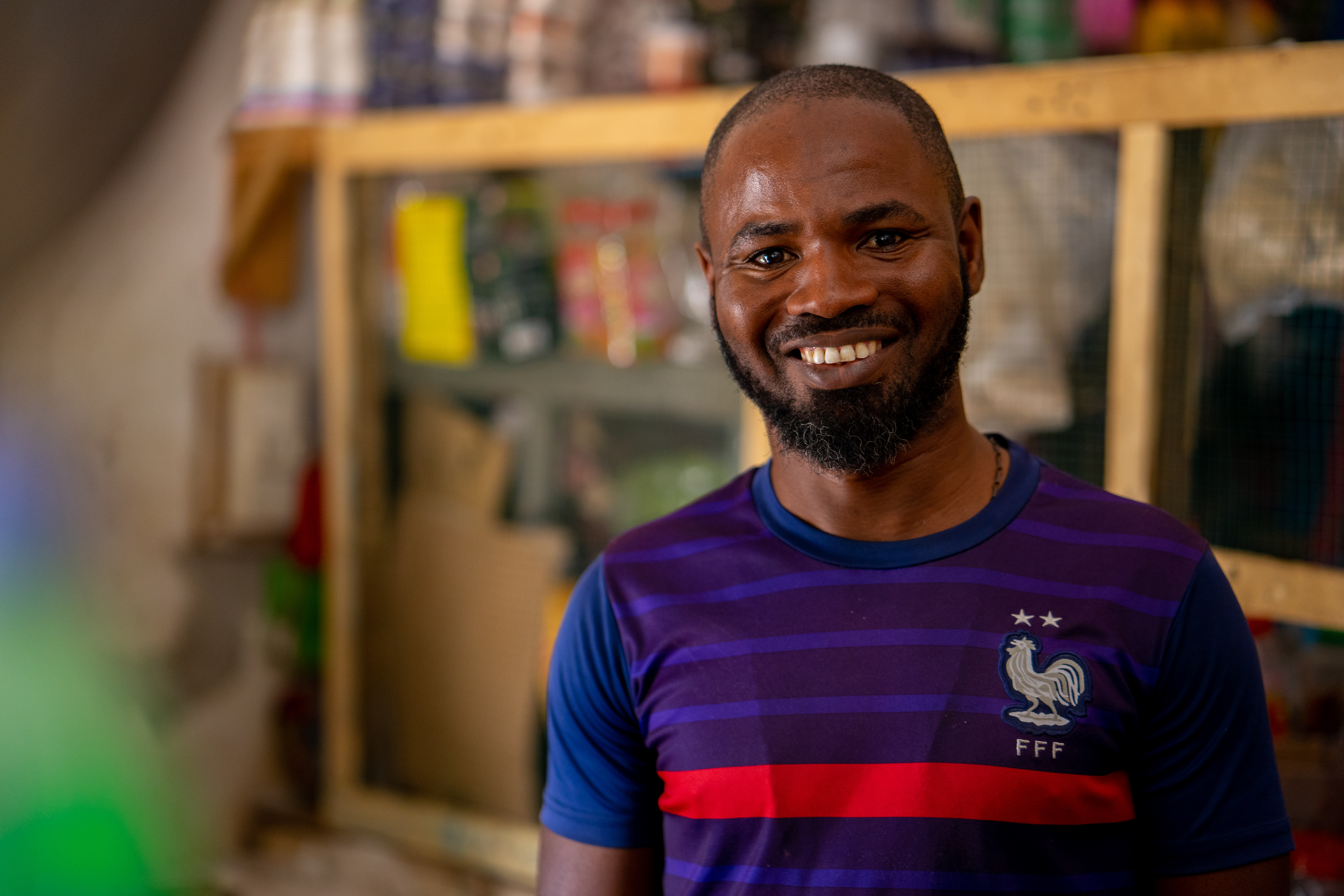 A shop keeping stands inside his shop in Senegal and smiles at the camera.